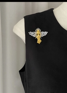 Detailed close-up of matte gold angel brooch with sparkling rhinestones on black fabric