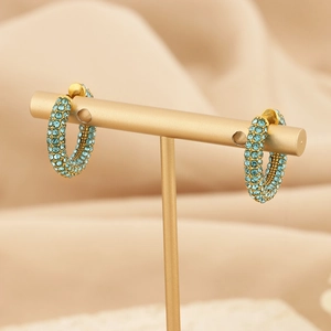Detail of C-shaped gold earrings with light blue crystals on a display stand