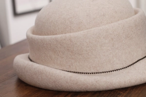 Detail of off-white wool felt cloche hat featuring a delicate dark beaded chain trim
