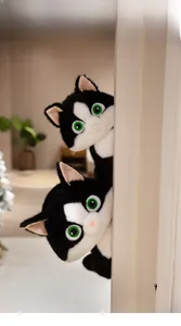 Close-up of cute black and white cat plush toys with green eyes peeking from a white door