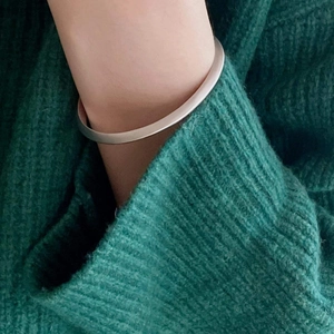 Detail of matte silver twisted cuff bracelet worn over a dark green knit sweater