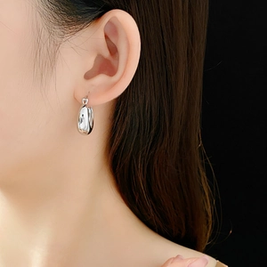 Close-up of polished silver U-shaped metal hoop earring worn by model on black background