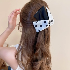 Detail of floral and black satin bow hair tie worn on a ponytail for elegant styling