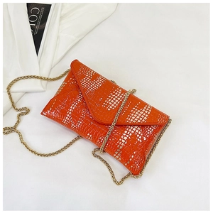 Detail of orange crocodile texture envelope bag with gold chain strap on white background