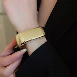 Detailed close-up of a wide polished gold wave cuff bracelet on a model wrist