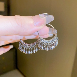 Macro shot of silver C-shaped metal tassel earrings with hanging water drop charms