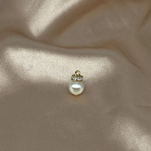 Golden pendant with round white pearl and sparkling stones on champagne silk background