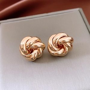Macro shot of gold knot stud earrings featuring a twisted textured metal design on silk