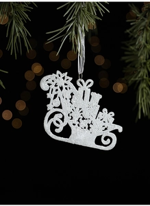 Sparkling white Christmas sleigh ornament hanging on pine branches with warm golden bokeh