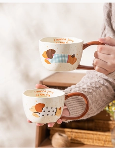 Detailed close-up showing hands holding two cute cartoon dog ceramic mugs with wavy rims