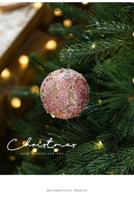 Detail of pink glitter Christmas ornament ball hanging on a green tree branch
