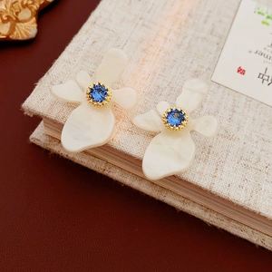 Vue macro de boucles d'oreilles fleurs en résine blanche avec zircon bleu sur un livre