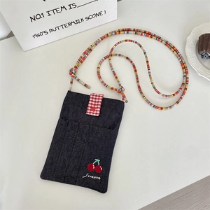 Detail of blue denim crossbody bag featuring red plaid flap and cute cherry embroidery