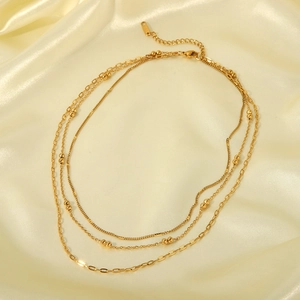 Multi-layer gold stainless steel necklace with bead accents on elegant silk background
