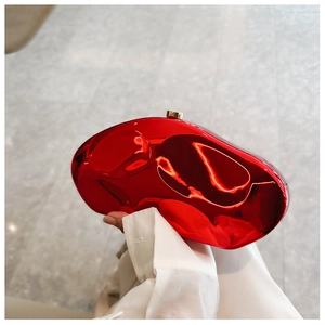 Close-up of a red mirror pebble clutch bag with gold clasp held against white sleeves