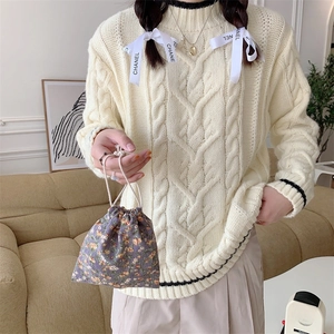 Off-white cable knit sweater with black trim and a purple floral corduroy drawstring bag
