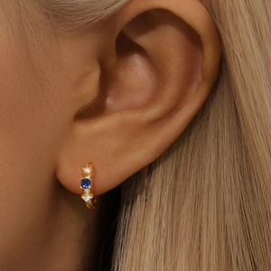 Macro shot of gold huggie hoop earring with pearl, blue gemstone and zircon on ear