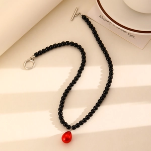 Primer plano de collar de cuentas negras con colgante de gota roja y cierre de barra plateado