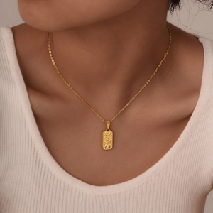 Close-up of a gold rectangle pendant necklace with sun and moon motifs on a model