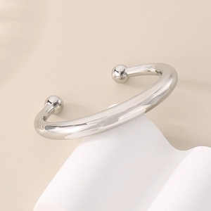 Gros plan d'un bracelet jonc argenté en forme de C avec embouts sphériques sur fond moderne