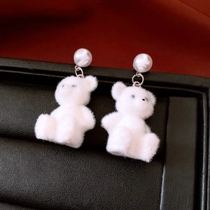 Detail van witte gevlokte berenoorbellen met parelstekers op zwarte display