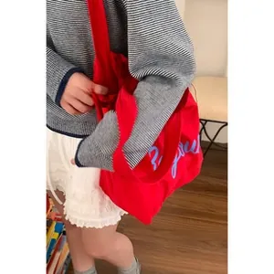 Detail of red canvas tote bag with blue script embroidery carried by model