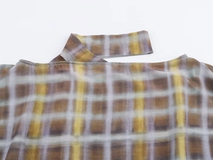 Gros plan sur l'encolure asymétrique d'un poncho à carreaux avec motif marron et jaune