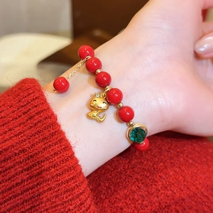Nahaufnahme eines roten Achat-Armbands mit goldenem Schlangenanhänger und grünem Stein.