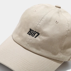 Macro detail of the 1987 black embroidery on a beige cotton canvas baseball cap