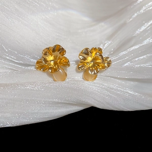 Detailed macro view of golden flower earrings with opal stone on white silk fabric