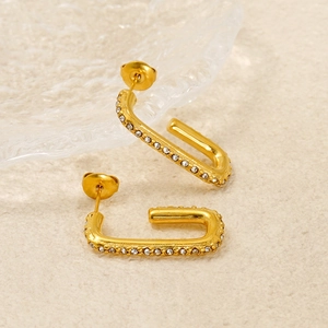 Close-up of gold U-shaped earrings with clear crystals on a glass tray background