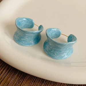 Detail of C-shaped blue marble enamel earrings with gold plating on a textured surface
