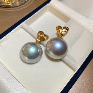 Macro detail of heart-shaped gold studs with large silver grey aurora pearls in a box