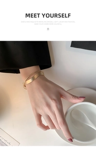 Dettaglio del bracciale a incrocio in oro opaco con design a onde indossato da una modella