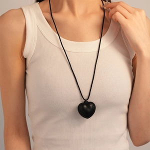 Gros plan du pendentif cœur en similicuir avec texture tressée sur un long collier noir