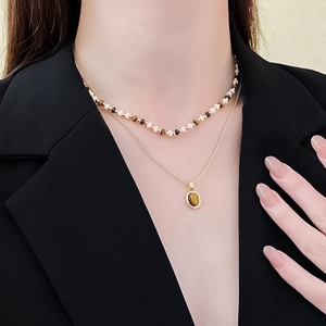 Close-up of a layered gold necklace featuring a bead string and tiger eye stone pendant