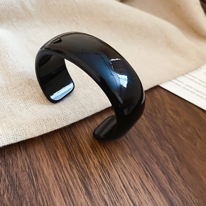 Gros plan d'un bracelet jonc ouvert en acrylique noir brillant sur une surface texturée