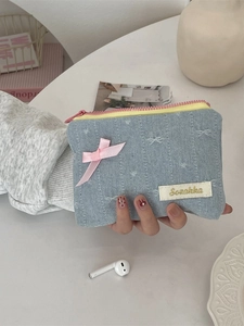 Denim coin purse with pink bow and gold logo held against a clean workspace