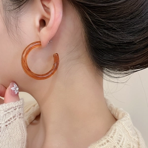 Close-up of a large amber acrylic C-shaped hoop earring worn on a model's ear