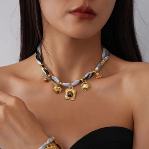 Close-up of fabric-wrapped chain necklace with gold heart, sun, and cherry pendants