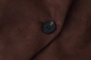 Macro detail of a black four-hole button on deep brown suede fabric of a V-neck blazer