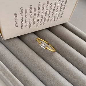 Detailed close-up of golden spiral band ring with square zircon in velvet box