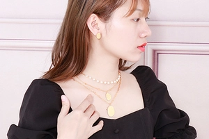 Close-up of a model wearing layered gold pearl necklaces and textured heart pendant earrings