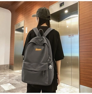 Man wearing a dark gray canvas backpack with a COOLBOY tag and astronaut pendant charm