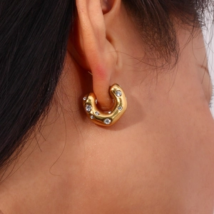 Close-up of chunky gold C-shaped earrings with inlaid clear zircon stones on ear