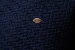 Macro shot of dark blue knit sweater texture with a premium bronze brand tag