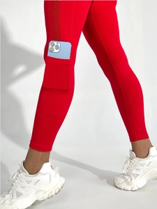 Détail de leggings de yoga rouges avec poche latérale pour téléphone et motifs découpés au laser