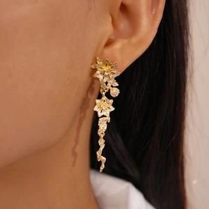Gros plan de boucles d'oreilles pendantes fleurs et feuilles en or mat sur un modèle