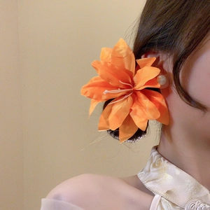 Detailed close-up of an orange silk lily hair clip worn elegantly on a model's hair