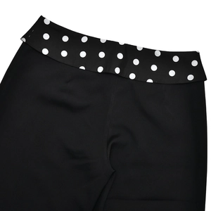 Detail of black straight-leg trousers with white polka dot folded waistband design